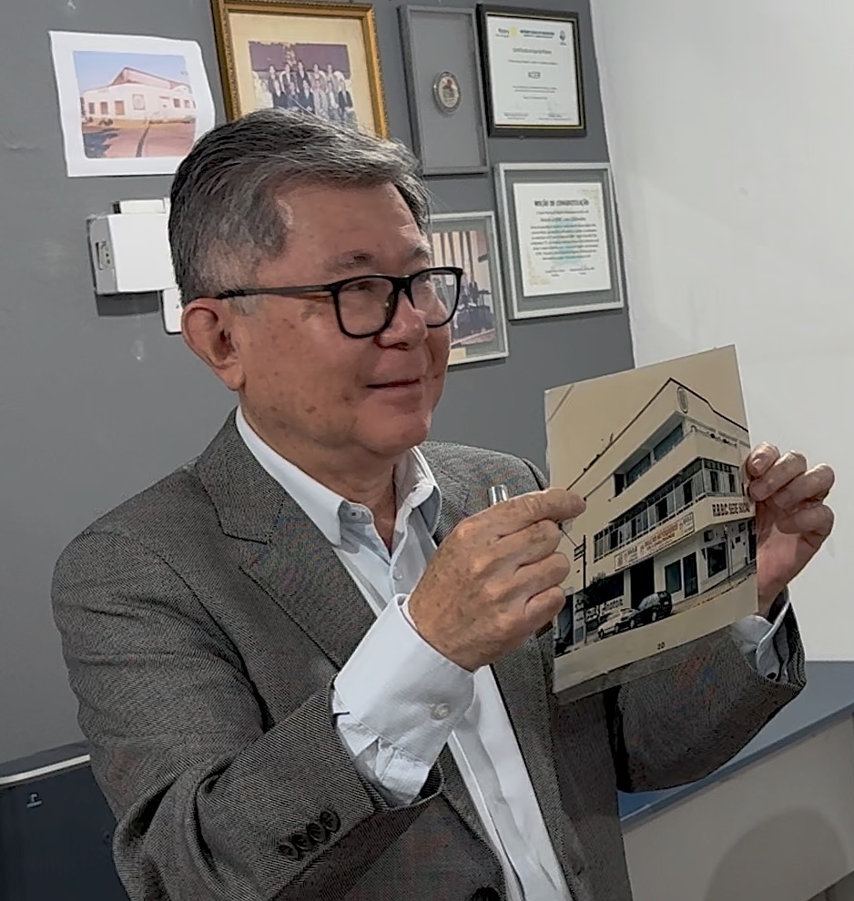 最初の会館の写真を見せながら歴史を説明する佐久川マリオACER会長