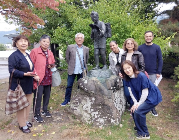 2025年10月11日 長野市若穂川田の川田小学校の金次郎像の前で記念撮影。左から橋本よし子、沼田はる、沼田清、二宮金次郎像、リアナ(かおり)、義家ミチコ、ジエゴ。手前は桂本久美子校長先生