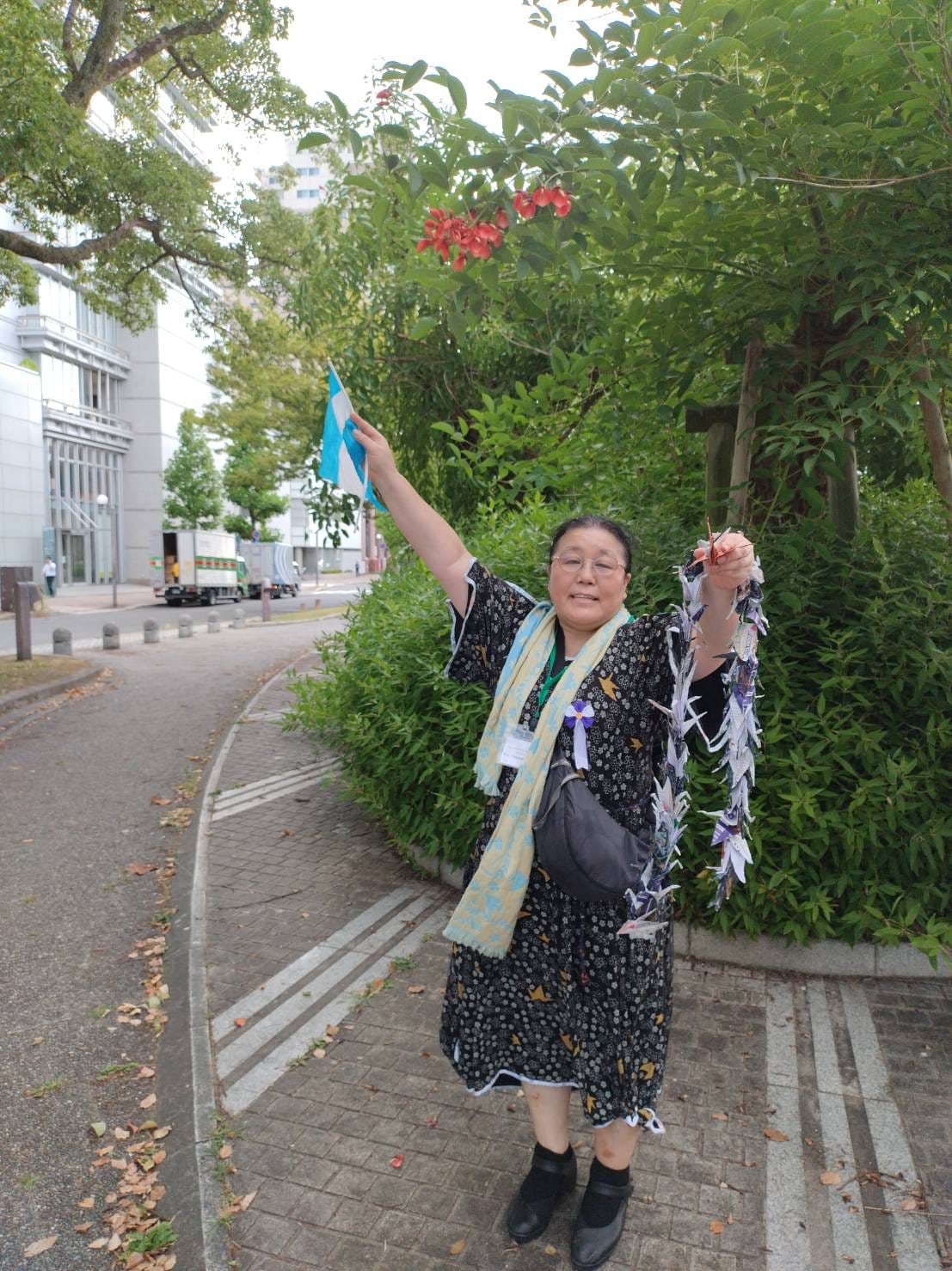 広島のアメリカデイゴ（後ろの赤い花）と著者の相川さん（2025年撮影）